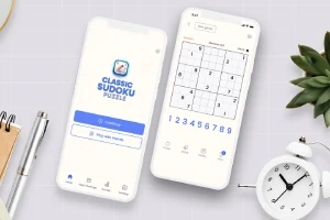 Två smartphones på ett bord med en anteckningsbok, en växt och ett litet väckarklocka, där den ena telefonen visar en öppningsskärm för en app och den andra visar ett spelpussel
