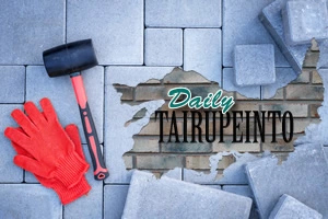 Röda arbetshandskar och en gummiklubba på stenläggning med trasigt område som avslöjar tegelvägg och texten Daily Tairupeinto