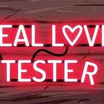 Neonskylt med texten REAL LOVE TESTER med ett hjärta istället för bokstaven O, mot en träbakgrund