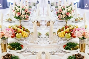 Ett elegant dukat bord med vit duk, dekorerat med blommor, fruktfat och vikta servetter