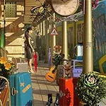 En tågplattform med färgglada resväskor, en gitarr, blommor och människor bredvid ett tåg under en stor klocka