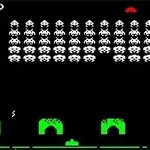 Svart bakgrund med rader av vita pixelerade figurer och gröna barriärer samt en röd flygande objekt högst upp