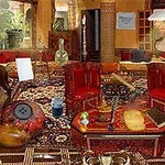 Ett rikt dekorerat rum med orientaliska mattor, röda stolar, och olika prylar utspridda över borden och golvet